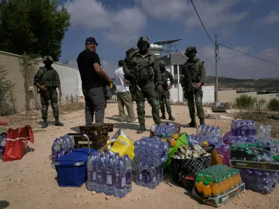 Activists accumulate food and water supplies in front of Israeli army soldiers who are blocking the road leading to the houses of three Palestinian families that have been besieged by Israeli settlers for six days, in the occupied West Bank village of Qusra, south of Nablus, Friday, Aug. 14, 2026. (AP Photo/Majdi Mohammed)