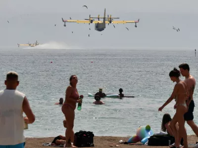 Beachgoers look at the firefighting airplanes scooping water from the Adriatic Sea during a wildfire near Omis, southern Croatia, Friday, Aug. 14, 2026. (AP Photo/Josko Ponos)