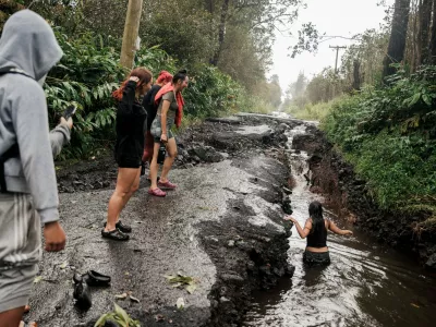 A teenager wades through a pool of water in a washed-out section of a damaged road in Mountain View, Hawaii, Sunday, Aug. 16, 2026, after a severe weather system went through the area. (Stephen Lam/San Francisco Chronicle via AP)
