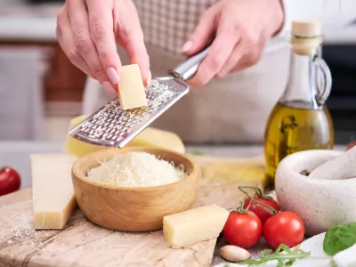 Woman grates Parmesan cheese on a wooden cutting board at domestic kitchen.