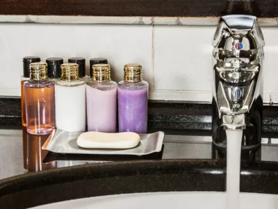 Water flows from the tap in the bathroom. Mini bottles of cosmetics on the table in the hotel room / Foto: Doroo