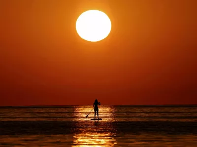 FILE PHOTO: A woman looks at the sunrise as she paddleboards on the Mediterranean Sea, in Barcelona, Spain July 2, 2025. REUTERS/Nacho Doce/File Photo