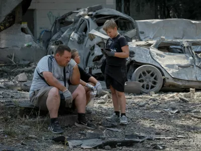 A family waits for a tow truck near destroyed cars at the site of yesterday's missile strike, amid Russia's attack on Ukraine, in Kyiv, Ukraine, August 21, 2026. REUTERS/Gleb Garanich