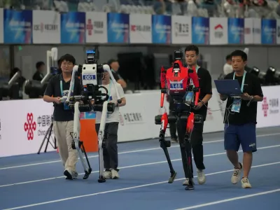 Technicians guide robots ahead of the 400m during the World Humanoid Robot Games in Beijing, Sunday, Aug. 23, 2026. (AP Photo/Achmad Ibrahim)