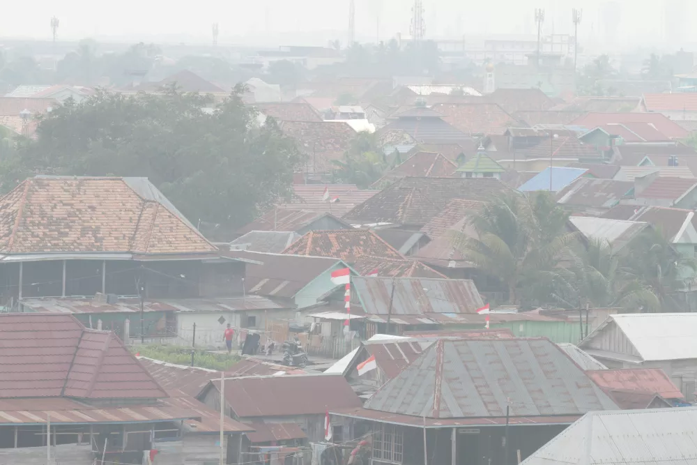 A man stands among houses as haze from wildfires blankets the city of Palembang, South Sumatra, Indonesia, Tuesday, Aug. 25, 2026. (AP Photo/Muhammad Hatta)