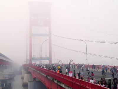 People walk along the Ampera Bridge as haze from wildfires blankets the city of Palembang, in South Sumatra, Indonesia, Sunday, Aug. 23, 2026. (AP Photo/Muhammad Fajri)