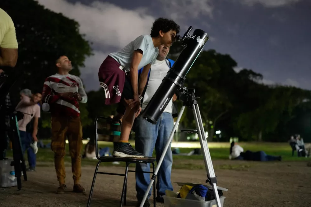 A boy looks at the moon through a telescope during a lunar eclipse in Caracas, Venezuela, Thursday, Aug. 27, 2026. (AP Photo/Ariana Cubillos)