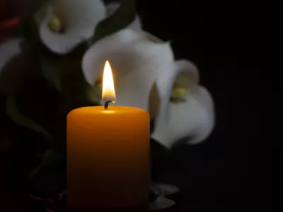 A close up of an orange candle and flame and lily flowers on a dark background.
