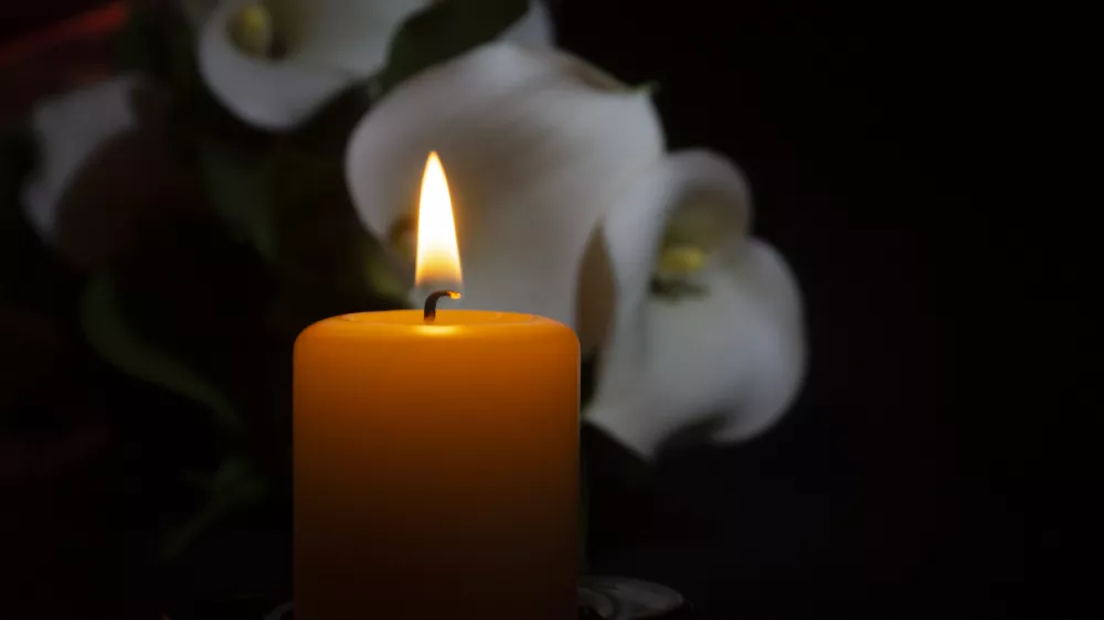 A close up of an orange candle and flame and lily flowers on a dark background.