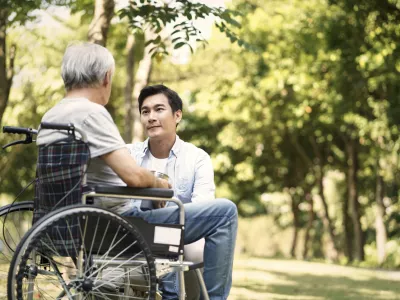 asian son talking to and comforting wheelchair bound father