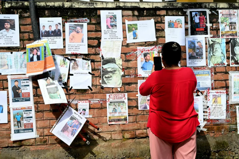 SENSITIVE MATERIAL. THIS IMAGE MAY OFFEND OR DISTURB A woman uses her phone to film photographs of missing and deceased people pasted on wall outside Tribhuvan University Teaching Hospital, following flash floods and mudslides, in Kathmandu, Nepal, August 31, 2026. REUTERS/Monika Malla