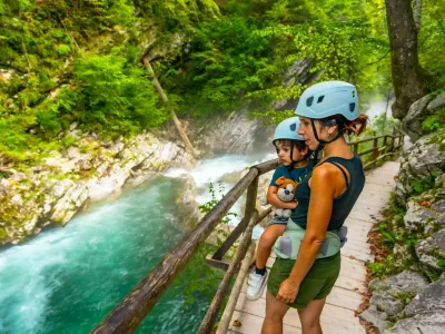 Mother carrying her child while wearing helmets and observing the radovna river flowing through the scenic vintgar gorge near bled, slovenia