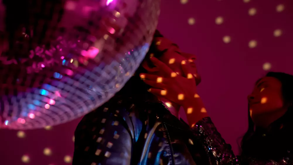 Drunk couple standing by disco ball, woman holding man face, passion and flirt