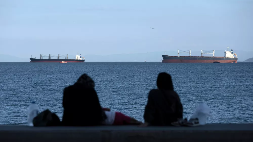 FILE - People sit in front of cargo ships anchor in the Marmara Sea await to cross the Bosphorus Straits in Istanbul, Turkey, on July 13, 2022. (AP Photo/Khalil Hamra, File)