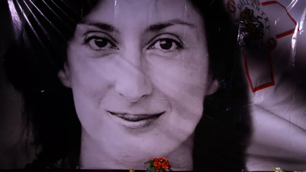 FILE - Flowers and a candle lie in front of a portrait of slain investigative journalist Daphne Caruana Galizia during a vigil outside the law courts in Valletta, Malta, Oct. 16, 2018. (AP Photo/Jonathan Borg, File)