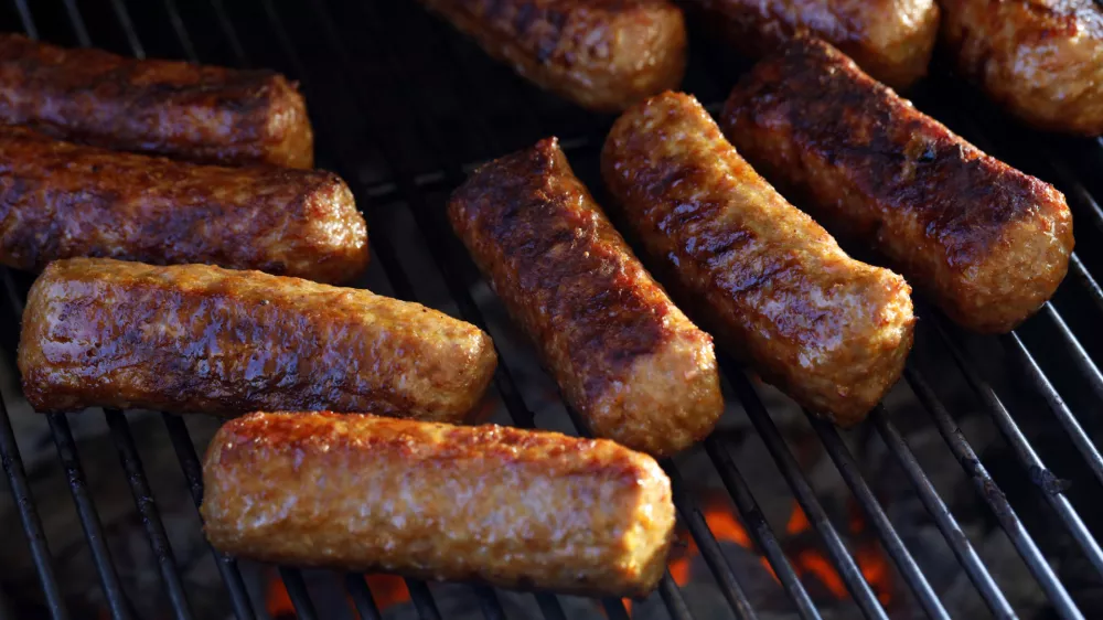 Close-up of roasted cevapi, cevapcici on the grill over glowing charcoal, traditional Balkan meat sausages on the bbq.