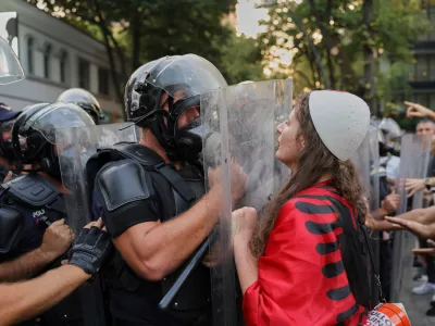 A woman draped in an Albanian flag clashes with police officers during ongoing demonstrations against plans for a luxury resort in a protected coastal area linked to Jared Kushner, U.S. President Donald Trump's son-in-law, in Tirana, Albania, Tuesday, Sept. 8, 2026. (AP Photo/Hameraldi Agolli)