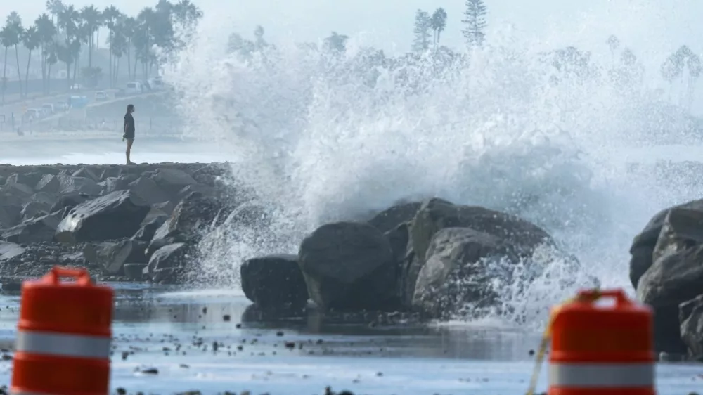 A person stands on a jetty as waves break over riprap and onto a beach parking lot in Carlsbad, California, U.S., September 8, 2026. REUTERS/Mike Blake