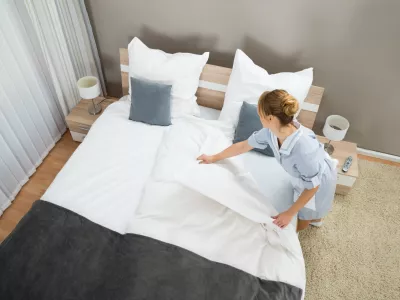 Young Female Housekeeper Changing Bedding In Hotel Room