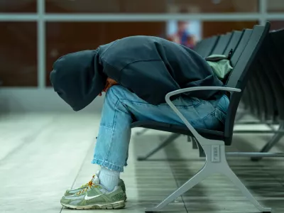 Side view of a tired passenger resting face down on waiting room chairs. The cinematic teal lighting creates a lonely, moody atmosphere. Ideal for travel delays, transit fatigue, airport lifestyle editorial, and modern youth culture concepts. Includes ample copy space on the left side of the frame. / Foto: Aleksei Gorovoi