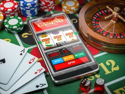 Casino online. Smartphone or mobile phone, slot machine, dice, cards and roulette on a green table in casino. 3d illustration / Foto: Bet_noire