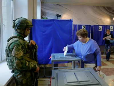 A woman casts her ballot next to a serviceman securing a poling station during Russia's parliamentary elections, in the course of Russia-Ukraine conflict in Donetsk, Russian-controlled Ukraine, September 18, 2026. REUTERS/Alexander Ermochenko