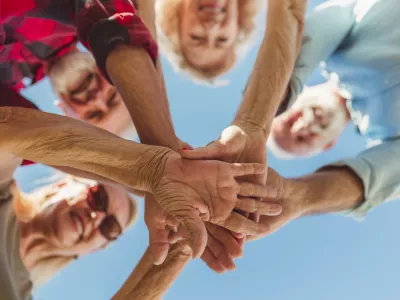 Low angle view of group of cheerful active senior people enjoying sunny summer day outdoors, gathered in circle, holding hands all together in the middle / Foto: Vladans Getty Images/istockphoto
