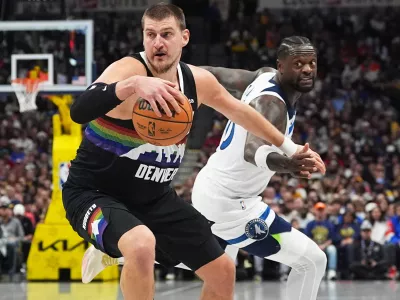 Denver Nuggets center Nikola Jokić, front, dribbles past Minnesota Timberwolves center Julius Randle in the first half of an NBA basketball game, Thursday, Dec. 25, 2025, in Denver. (AP Photo/David Zalubowski)