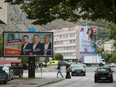 People walk past a campaign billboard featuring Democratic Front (Demokratska fronta) members Arman Zalihic, Zeljko Komsic and Zoran Mikulic, with a billboard featuring Darijana Filipovic, a candidate of the Croat Democratic Union of Bosnia and Herzegovina (HDZ BiH) for the Croat member of the Presidency of Bosnia and Herzegovina, in the background, ahead of the 2026 general election, in Mostar, Bosnia and Herzegovina, September 25, 2026. REUTERS/Amel Emric