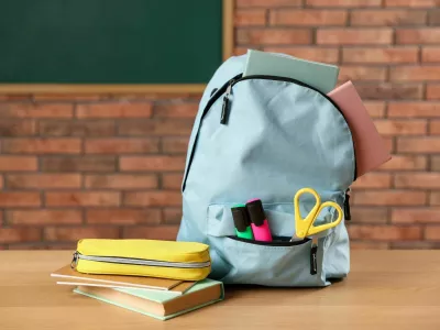 Light blue backpack with different stationery, pencil case and book on desk in classroom / Foto: Olga Yastremska
