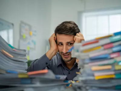 Tired Hispanic employee dealing with overwhelming workloads indoors, experiencing anxiety and pain from work-related challenges and deadlines.