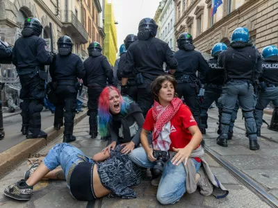 Demonstrators get shelter behind the police after clashes occurred during a protest against the high cost of living, in Milan, Italy, Saturday Oct. 17, 2026. (Stefano Porta/LaPresse via AP)