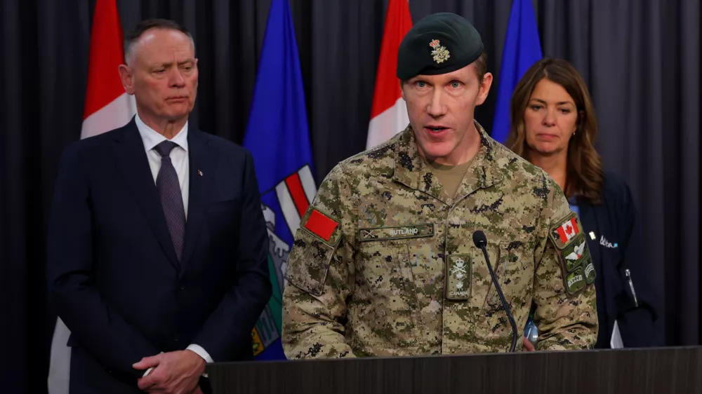 Major-General L.W. Rutland, center, speaks as Canada National Defence Minister David McGuinty, left, and Alberta Premier Danielle Smith, right, listen during a news conference in Edmonton, Alberta, Sunday, Oct. 18, 2026. (James Maclennan/The Canadian Press via AP)