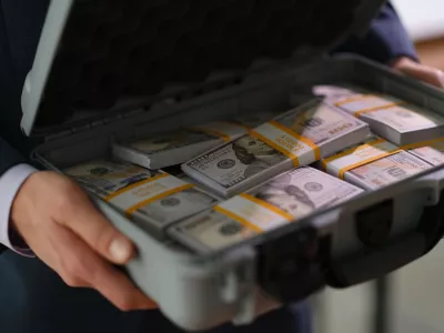 Businessman in suit holding suitcase full of currency money closeup. Profitable financial deals concept