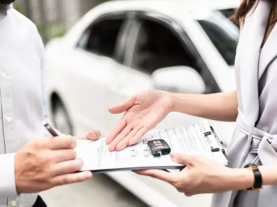 Automotive business, car sale or rental concept: Happy customer with car dealer agent making deal and signing on agreement document contract in auto showroom or car dealer office.
