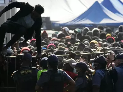 FILE - A Malawian migrant jumps over a barricade as the police officer manage the queue for their deportation at a temporary centre, in Durban, South Africa, Thursday, June 18, 2026. (AP Photo/Themba Hadebe, File)