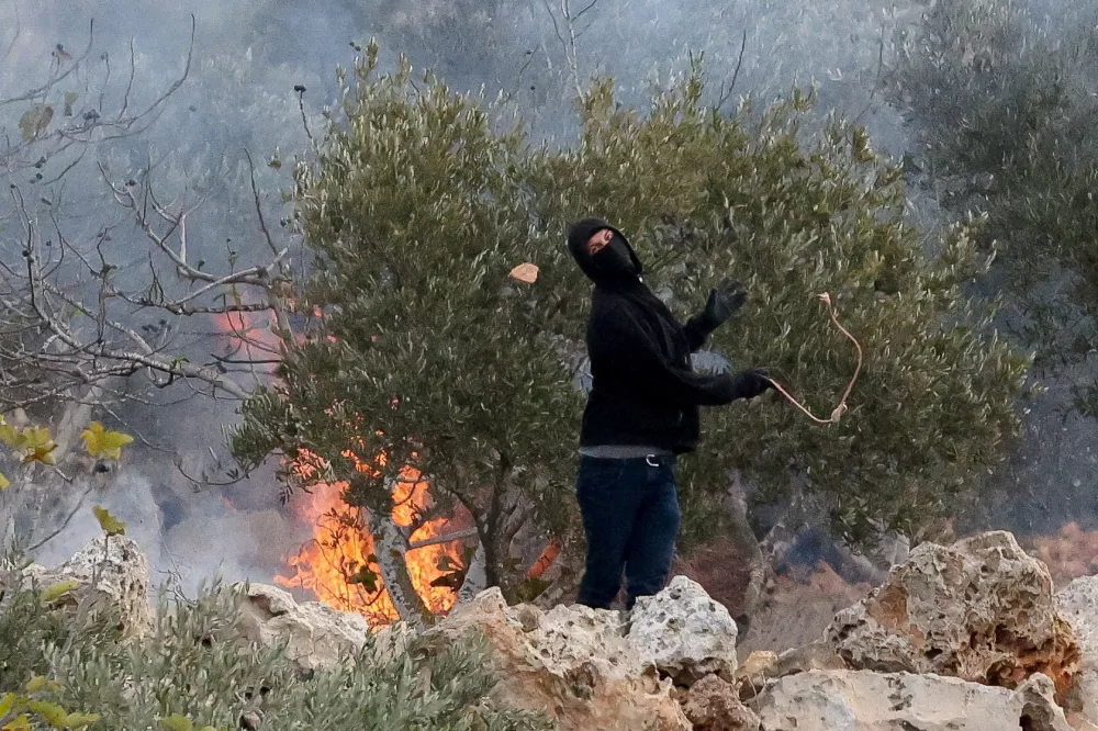 FILE PHOTO: An Israeli settler casts a stone towards Palestinians, next to a fire, amid clashes during Palestinians' olive harvest in Abu Falah near Ramallah in the Israeli-occupied West Bank, October 16, 2026. REUTERS/Ammar Awad/File Photo