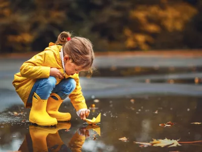 happy child girl with umbrella and paper boat in a puddle in autumn on nature
