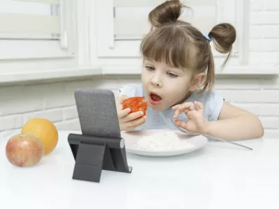 kid girl eating food and watching cartoons on a smartphone