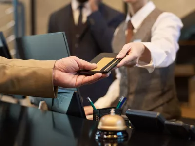 Receptionist taking credit card from guest at hotel reception for transaction processing. Elegant setup with polished service tools like bell and pen holder visible on counter