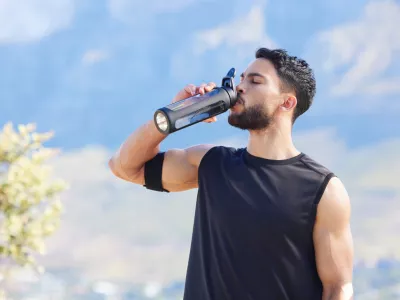 Fitness, blue sky and man drinking water from bottle to refresh and relax after workout, running or sports training. Cardio runner, exercise and thirsty young person with liquid drink for hydration