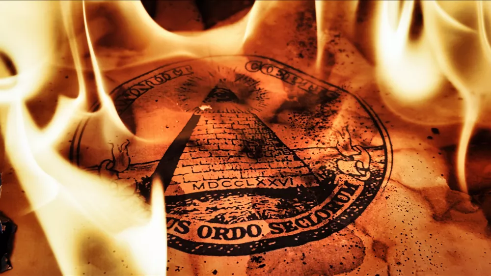 An ancient burnt parchment paper featuring the printed Masonic All Seeing Eye pyramid symbol, dramatically engulfed and illuminated by real blazing fire flames creating a mysterious, occult atmosphere for secret society concepts.