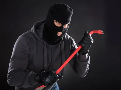 Portrait Of A Burglar Wearing Balaclava Holding Crowbar On Black Background