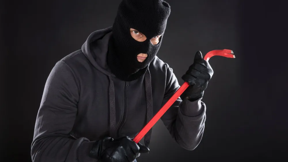 Portrait Of A Burglar Wearing Balaclava Holding Crowbar On Black Background