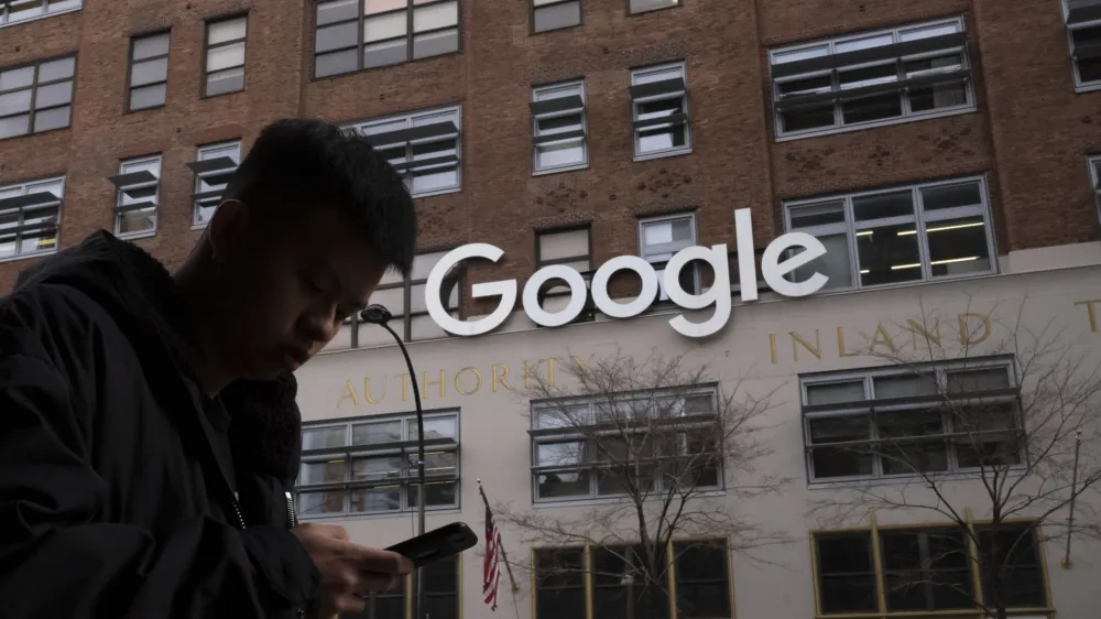 FILE - In this Dec. 17, 2018, file photo a man using a mobile phone walks past Google offices in New York. Google says it plans to launch a video-game streaming platform called Stadia, positioning itself to take on the traditional video-game business. (AP Photo/Mark Lennihan, File)