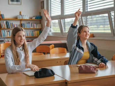 Two teen female pupils raising their hands to answer the question in the classroom. Back to school concept.