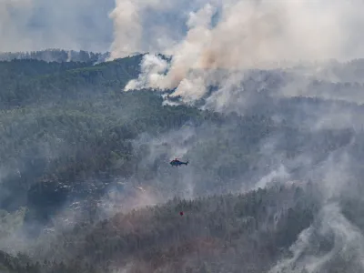 28 July 2022, Saxony, Schmilka: A cargo helicopter from Austria flies with an external water tank to extinguish a forest fire at the Saxon Switzerland National Park. Photo: Robert Michael/dpa