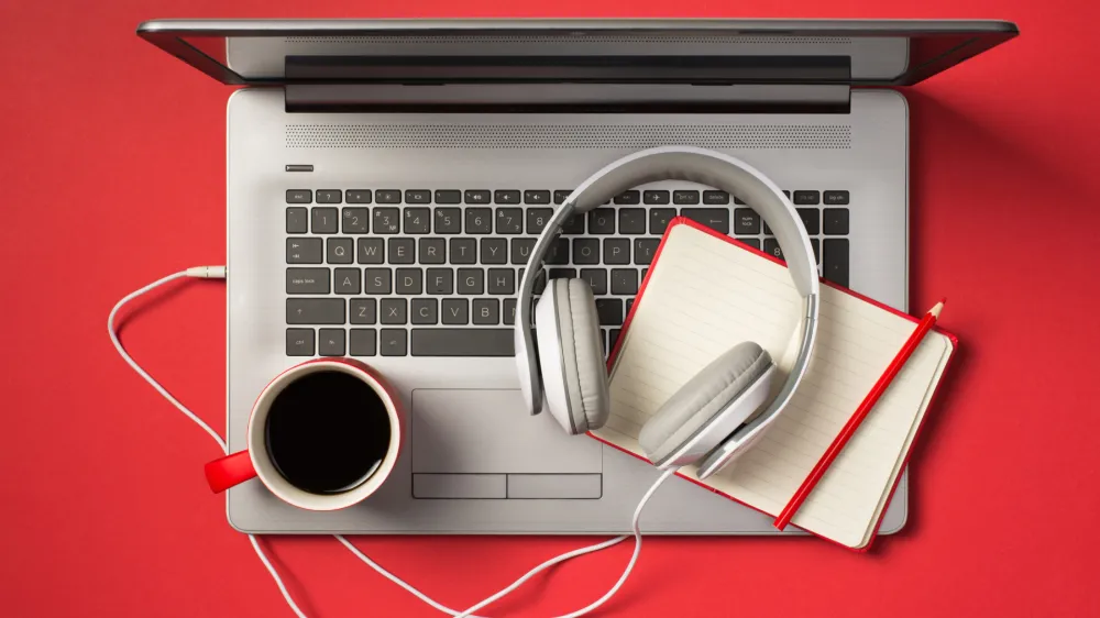 Above photo of grey laptop cup of coffee notebook with pencil and headphones isolated on the red backdrop