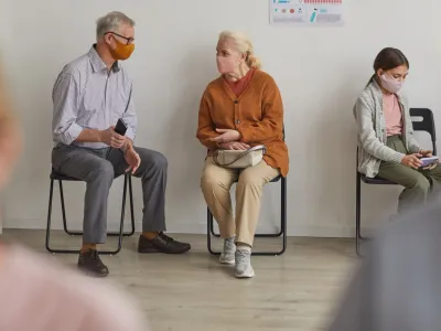 Full length portrait of senior couple wearing masks while waiting in line at clinic or vaccination center, copy space