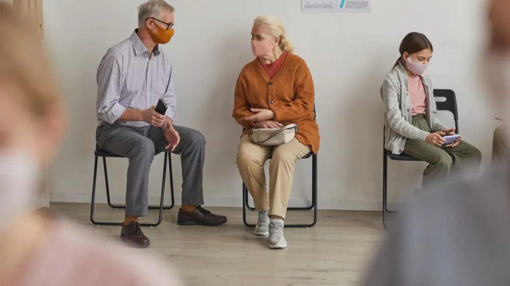 Full length portrait of senior couple wearing masks while waiting in line at clinic or vaccination center, copy space